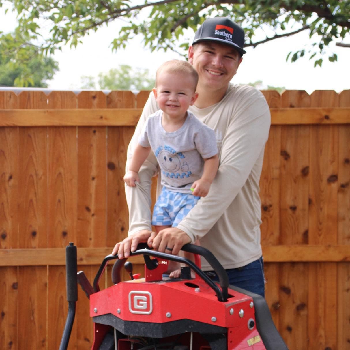 Dolen smiling with his young son as they sit together on a red mower